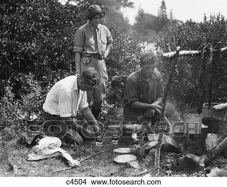1920S Woman Watching Two Men Around Campfire One Cooking In Skillet Other Opening Cans Of Soup Mersey River Nova Scotia Canada View Large Photo Image Picture - 1920S Woman Watching Two Men Around Campfire One Cooking In Skillet Other Opening Cans Of Soup Mersey River Nova Scotia Canada. Fotosearch