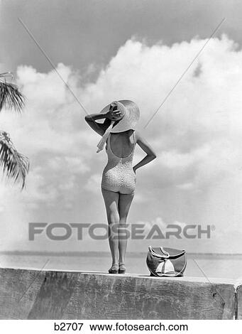 1930s 1940s ANONYMOUS WOMAN BACK VIEW FULL LENGTH STANDING ON TROPICAL BEACH WALL HOLDING ON TO HER AT IN BREEZE View Large Photo Image Stock Photo - 1930s 1940s ANONYMOUS WOMAN BACK VIEW FULL LENGTH STANDING ON TROPICAL BEACH WALL HOLDING ON TO HER AT IN BREEZE. Fotosearch