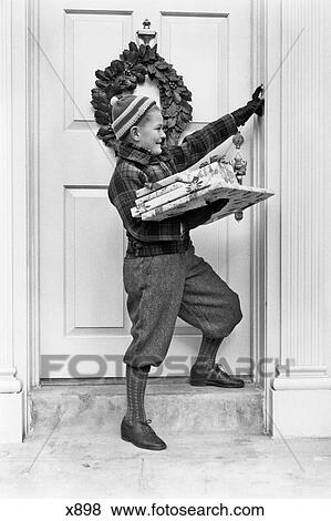 1930s 1940s BOY HOLDING WRAPPED PACKAGES RINGING BELL ON DOOR WITH CHRISTMAS WREATH View Large Photo Image Stock Photo - 1930s 1940s BOY HOLDING WRAPPED PACKAGES RINGING BELL ON DOOR WITH CHRISTMAS WREATH. Fotosearch