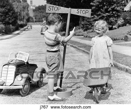 Stock Photo - 1930s 1940s BOY PLAYING TRAFFIC COP POINTING TO STOP SIGN HALTING GIRL WITH WHEELBARROW. Fotosearch