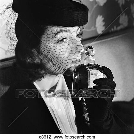 Stock Image - 1930S 1940S Elegant Upscale Woman Wearing Hat With Veil Sniffing Bottle Of Whimsy Perfume. Fotosearch
