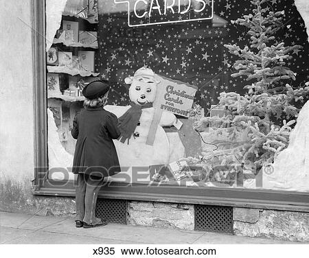 Stock Photography - 1930s 1940s LITTLE GIRL LOOK INTO CARD SHOP WINDOW WITH CHRISTMAS DECORATIONS AND SNOWMAN DISPLAY. Fotosearch