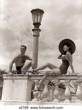 1930s 1940s MAN WOMAN SUN HAT COUPLE BATHING SUITS SITTING ON BALUSTRADE WALL TROPICAL VACATION HOTEL MIAMI BEACH FLORIDA USA View Large Photo Image Stock Photo - 1930s 1940s MAN WOMAN SUN HAT COUPLE BATHING SUITS SITTING ON BALUSTRADE WALL TROPICAL VACATION HOTEL MIAMI BEACH FLORIDA USA. Fotosearch