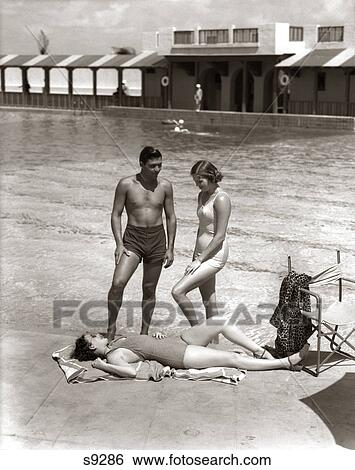 1930s 1940s TWO WOMEN SUNBATHING AND MAN AT HOTEL SWIMMING POOL SIDE WEARING BATHING SUITS VACATION MIAMI BEACH FLORIDA USA View Large Photo Image Stock Photograph - 1930s 1940s TWO WOMEN SUNBATHING AND MAN AT HOTEL SWIMMING POOL SIDE WEARING BATHING SUITS VACATION MIAMI BEACH FLORIDA USA. Fotosearch