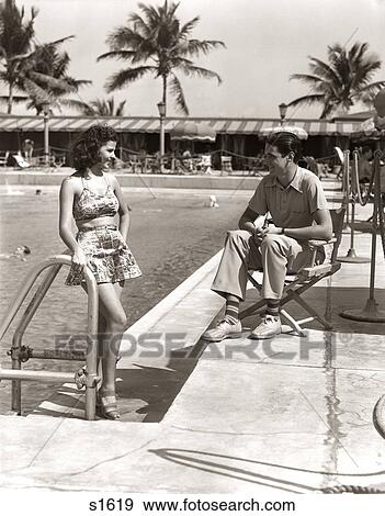 1930s COUPLE TROPICAL HOTEL SWIMMING POOL SIDE WOMAN BATHING SUIT MAN SITTING DIRECTORS CHAIR CASUAL CLOTHES MIAMI BEACH FL USA View Large Photo Image Stock Photo - 1930s COUPLE TROPICAL HOTEL SWIMMING POOL SIDE WOMAN BATHING SUIT MAN SITTING DIRECTORS CHAIR CASUAL CLOTHES MIAMI BEACH FL USA. Fotosearch