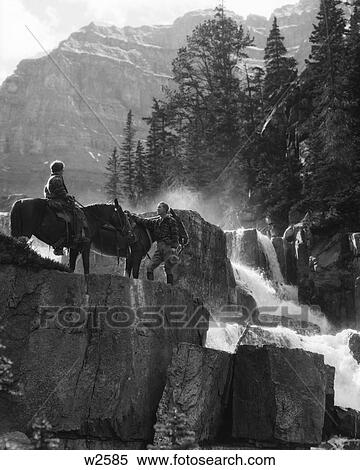 1930s COUPLE WOMAN ON HORSE MAN STANDING BY HORSE NEAR WATERFALL IN PINE FOREST GIANTS STEPS PARADISE VALLEY ALBERTA CANADA View Large Photo Image Stock Photography - 1930s COUPLE WOMAN ON HORSE MAN STANDING BY HORSE NEAR WATERFALL IN PINE FOREST GIANTS STEPS PARADISE VALLEY ALBERTA CANADA. Fotosearch