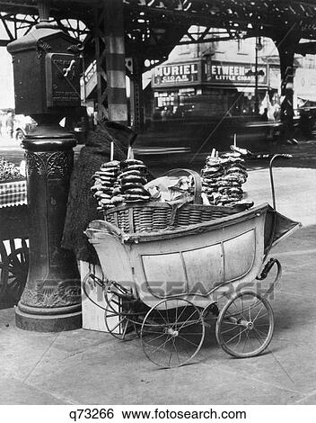 Stock Photograph - 1930s DEPRESSION SCENE OF PRETZEL VENDOR CART MADE FROM A BABY CARRIAGE NEXT TO FIRE ALARM BOX NEW YORK CITY USA. Fotosearch