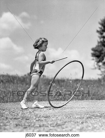 1930s GIRL OUTDOORS ROLLING A HOOP PLAYING HOOP AND STICK GAME View Large Photo Image Stock Photo - 1930s GIRL OUTDOORS ROLLING A HOOP PLAYING HOOP AND STICK GAME. Fotosearch