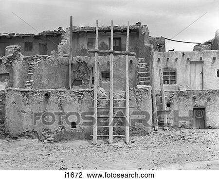 Stock Image - 1930s KIVA LADDER AND ADOBE BUILDING ARCHITECTURE ACOMA PUEBLO NEW MEXICO USA. Fotosearch