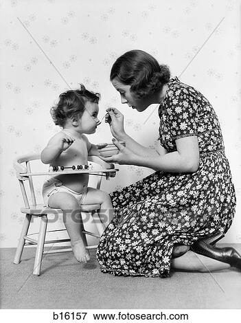 1930S Kneeling Mother Feeding Baby Sitting In Chair View Large Photo Image Stock Photo - 1930S Kneeling Mother Feeding Baby Sitting In Chair. Fotosearch