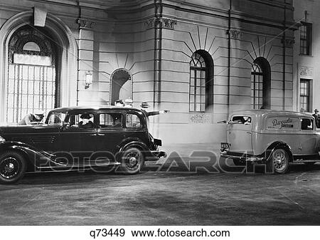 Stock Photo - 1930S Movie Still Of Nighttime Shootout Between Gangsters In A Parked Car And A Passing Panel Truck. Fotosearch