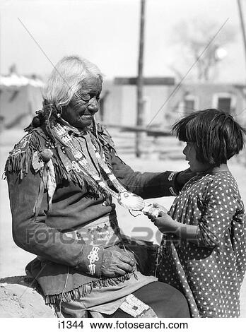 1930s NATIVE AMERICAN CHILD ADMIRING BEADED NECKLACE OF ELDERLY INDIAN MAN SANTA CLARA PUEBLO NEW MEXICO USA View Large Photo Image Picture - 1930s NATIVE AMERICAN CHILD ADMIRING BEADED NECKLACE OF ELDERLY INDIAN MAN SANTA CLARA PUEBLO NEW MEXICO USA. Fotosearch