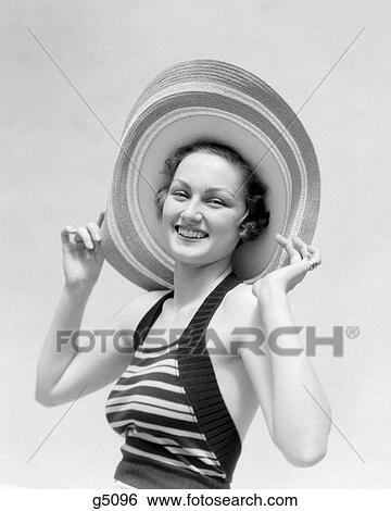 1930s PORTRAIT SMILING WOMAN IN STRAW HAT AND STRIPED HALTER TOP HOLDING THE HAT ON WITH HER HANDS SUN HAT LOOKING AT CAMERA View Large Photo Image Stock Photograph - 1930s PORTRAIT SMILING WOMAN IN STRAW HAT AND STRIPED HALTER TOP HOLDING THE HAT ON WITH HER HANDS SUN HAT LOOKING AT CAMERA. Fotosearch