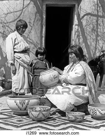 Stock Photo - 1930S Pueblo Woman Decorating Pottery An Older Woman & Child Looking On From Side. Fotosearch