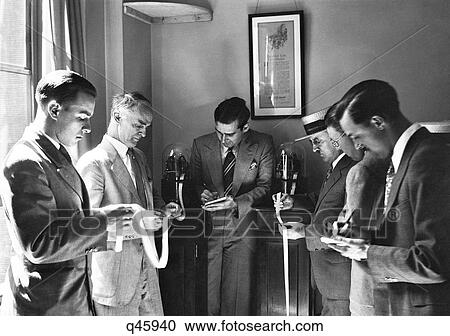 Stock Image - 1930S Six Engrossed Investors And Stock Brokers Reading Paper Ticker Tape Invented In 1867 By Edward Calahan New York City Usa. Fotosearch