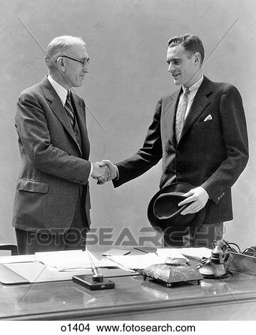 1930s TWO MEN STANDING AT DESK IN OFFICE SHAKING HANDS View Large Photo Image Picture - 1930s TWO MEN STANDING AT DESK IN OFFICE SHAKING HANDS. Fotosearch