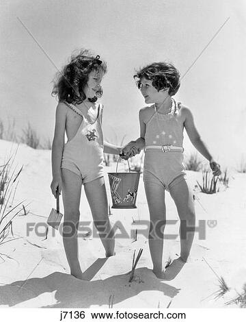 1930s TWO SMILING GIRLS SISTERS FRIENDS HOLDING HANDS AND SAND PAIL AND SHOVEL WALKING ON SAND DUNE View Large Photo Image Stock Photograph - 1930s TWO SMILING GIRLS SISTERS FRIENDS HOLDING HANDS AND SAND PAIL AND SHOVEL WALKING ON SAND DUNE. Fotosearch