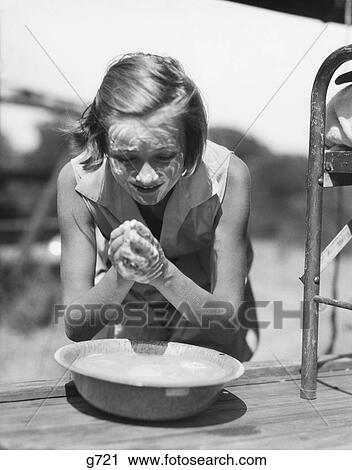 Stock Image - 1930S Young Girl Leaning Over Bowl Washing Hands And Face With Soap At Summer Camp Outdoors. Fotosearch