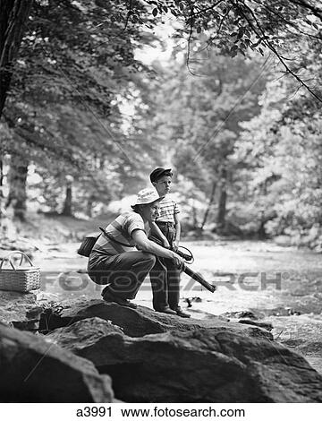 1940s 1950s FATHER AND BOY BY SIDE OF STREAM PICNIC BASKET MAN KNEELING HOLDING FISHING GEAR SUMMERTIME View Large Photo Image Stock Image - 1940s 1950s FATHER AND BOY BY SIDE OF STREAM PICNIC BASKET MAN KNEELING HOLDING FISHING GEAR SUMMERTIME. Fotosearch