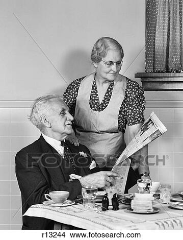 1940s ELDERLY COUPLE MAN WOMAN IN KITCHEN MAN SITTING AT TABLE WOMAN LOOKING OVER HIS SHOULDER READING NEWSPAPER View Large Photo Image Picture - 1940s ELDERLY COUPLE MAN WOMAN IN KITCHEN MAN SITTING AT TABLE WOMAN LOOKING OVER HIS SHOULDER READING NEWSPAPER. Fotosearch