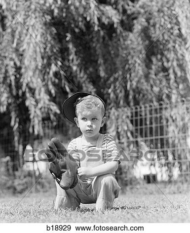 Stock Photo - 1940s SMALL SERIOUS BLOND BOY HOLDING A BASEBALL MITT WEARING BASEBALL CAP IN THE GRASS. Fotosearch
