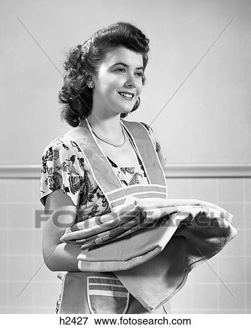 1940s SMILING BRUNETTE HOUSEWIFE WEARING APRON HOLDING STACK OF FOLDED LAUNDRY View Large Photo Image Stock Photo - 1940s SMILING BRUNETTE HOUSEWIFE WEARING APRON HOLDING STACK OF FOLDED LAUNDRY. Fotosearch