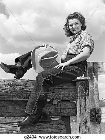 1940S Smiling Brunette Woman Wearing Jeans Western Wear Holding Cowboy Hat Sitting On Wooden Fence Looking At Camera View Large Photo Image Picture - 1940S Smiling Brunette Woman Wearing Jeans Western Wear Holding Cowboy Hat Sitting On Wooden Fence Looking At Camera. Fotosearch