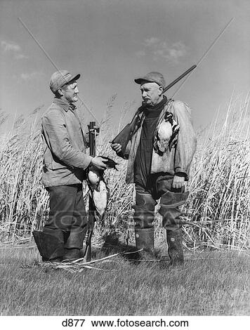 Stock Photo - 1940S Two Men Duck Hunting Standing In Marsh Grass Talking Holding Shotguns And Dead Ducks. Fotosearch