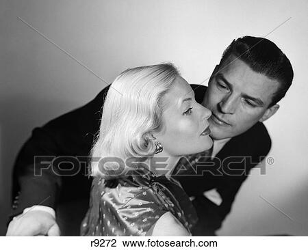 1950S 1960S Couple Aloof Woman Pretty Blonde Hair Elegant Earrings Fashion Profile About To Be Kissed By Man Standing Behind Her View Large Photo Image Stock Image - 1950S 1960S Couple Aloof Woman Pretty Blonde Hair Elegant Earrings Fashion Profile About To Be Kissed By Man Standing Behind Her. Fotosearch