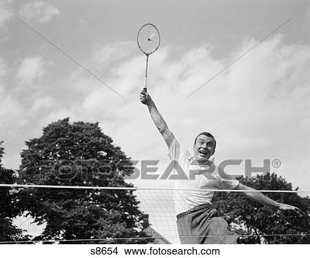 1950S 1960S Man Playing Badminton Jumping Up Arm Extended Racquet About To Hit Shuttlecock Birdie Wacky Funny Extreme Effort Lob View Large Photo Image Picture - 1950S 1960S Man Playing Badminton Jumping Up Arm Extended Racquet About To Hit Shuttlecock Birdie Wacky Funny Extreme Effort Lob. Fotosearch