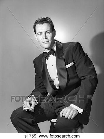 1950s 1960s MAN WEARING TUXEDO HOLDING CIGARETTE LOOKING AT CAMERA PORTRAIT View Large Photo Image Stock Photo - 1950s 1960s MAN WEARING TUXEDO HOLDING CIGARETTE LOOKING AT CAMERA PORTRAIT. Fotosearch