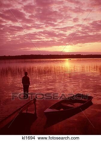 1950s 1960s OLDER BOY STANDING ON END OF DOCK LOOKING INTO SUNSET OVER LAKE View Large Photo Image Picture - 1950s 1960s OLDER BOY STANDING ON END OF DOCK LOOKING INTO SUNSET OVER LAKE. Fotosearch