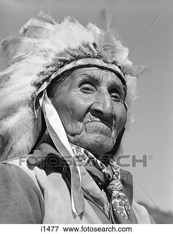 Stock Photo - 1950s 1960s PORTRAIT NATIVE AMERICAN CHEROKEE INDIAN SENIOR MAN WEARING FEATHER HEADDRESS LOOKING AT CAMERA NORTH CAROLINA USA. Fotosearch