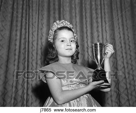 1950S 1960S Young Girl Standing With Trophy Loving Cup Wearing Tiara Pretty Dress Winner Of Beauty Pageant Looking At Camera View Large Photo Image Stock Photography - 1950S 1960S Young Girl Standing With Trophy Loving Cup Wearing Tiara Pretty Dress Winner Of Beauty Pageant Looking At Camera. Fotosearch