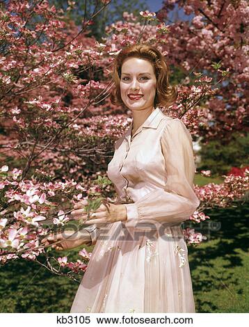 1950s 1960s YOUNG RED HAIRED WOMAN POSING UNDER BLOSSOMING DOGWOOD TREE LOOKING AT CAMERA View Large Photo Image Stock Photography - 1950s 1960s YOUNG RED HAIRED WOMAN POSING UNDER BLOSSOMING DOGWOOD TREE LOOKING AT CAMERA. Fotosearch