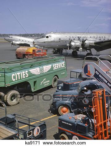 Stock Image - 1950s COLONIAL AIRLINES AIRPLANE ON TARMAC WITH GASOLINE TRUCKS IN FOREGROUND LAGUARDIA AIRPORT NEW YORK USA. Fotosearch