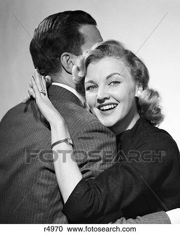 1950S Couple Arm In Arm Embrace Hug Man Face Hidden By Woman Smiling Displaying New Engagement Diamond Ring On Her Finger View Large Photo Image Stock Image - 1950S Couple Arm In Arm Embrace Hug Man Face Hidden By Woman Smiling Displaying New Engagement Diamond Ring On Her Finger. Fotosearch