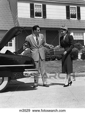 Stock Photo - 1950s COUPLE PACKING LUGGAGE IN CAR TRUNK FOR VACATION TRIP. Fotosearch