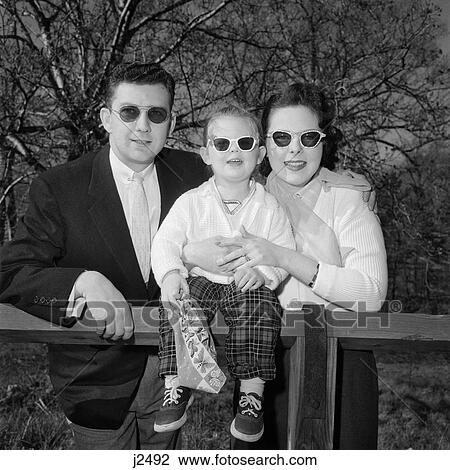 Stock Image - 1950S Family Father Mother Daughter At Fence Wearing Dark Sunglasses Looking At Camera. Fotosearch