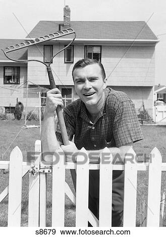 Stock Photo - 1950S Man In Plaid Shirt In Backyard Leaning On White Picket Fence With Rake In Hand. Fotosearch