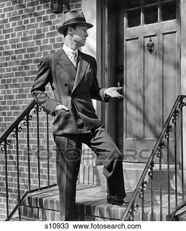 Stock Image - 1950s MAN SUIT TIE HAT SALESMAN STANDING REJECTED AT FRONT DOOR ON FRONT STOOP OF BRICK BUILDING. Fotosearch