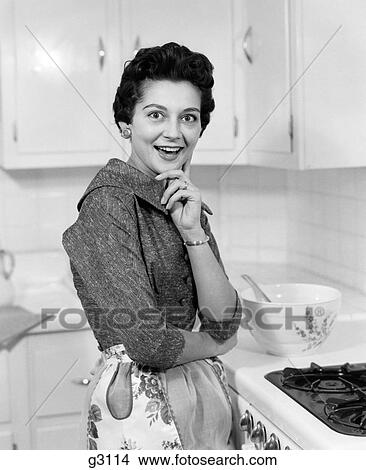 1950S Smiling Brunette Woman Housewife Beside Stove Wearing Apron In Kitchen Surprised Facial Expression Looking At Camera View Large Photo Image Picture - 1950S Smiling Brunette Woman Housewife Beside Stove Wearing Apron In Kitchen Surprised Facial Expression Looking At Camera. Fotosearch