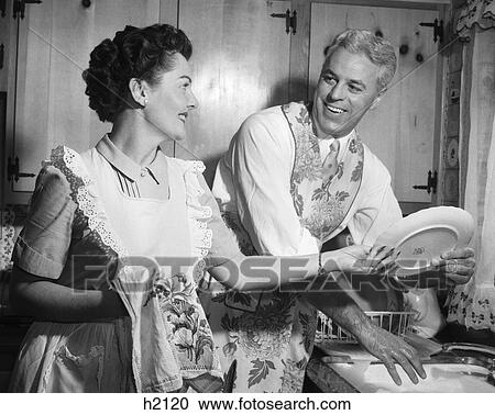 1950S Smiling Husband In Apron In Kitchen Washing Dishes As Happy Wife Dries View Large Photo Image Stock Image - 1950S Smiling Husband In Apron In Kitchen Washing Dishes As Happy Wife Dries. Fotosearch