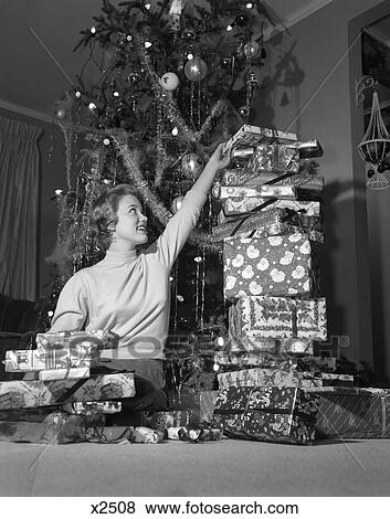 1950S Smiling Young Woman Sitting Under Christmas Tree Stacking Tall Pile Of Gift Wrapped Presents View Large Photo Image Stock Photo - 1950S Smiling Young Woman Sitting Under Christmas Tree Stacking Tall Pile Of Gift Wrapped Presents . Fotosearch