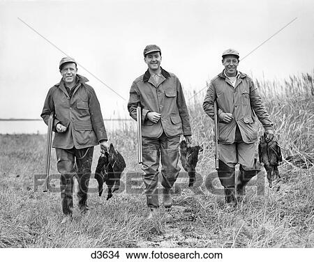 1950s THREE MEN LOOKING AT CAMERA HOLDING SHOTGUNS WALKING THROUGH GRASSY WETLANDS EACH CARRYING BRACE OF DUCKS View Large Photo Image Picture - 1950s THREE MEN LOOKING AT CAMERA HOLDING SHOTGUNS WALKING THROUGH GRASSY WETLANDS EACH CARRYING BRACE OF DUCKS. Fotosearch