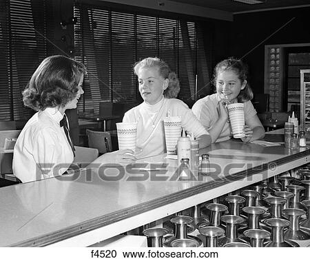 1950s THREE PRE-TEEN GIRLS DRINKING MILKSHAKES SITTING TALKING AT SODA FOUNTAIN COUNTER View Large Photo Image Stock Image - 1950s THREE PRE-TEEN GIRLS DRINKING MILKSHAKES SITTING TALKING AT SODA FOUNTAIN COUNTER. Fotosearch