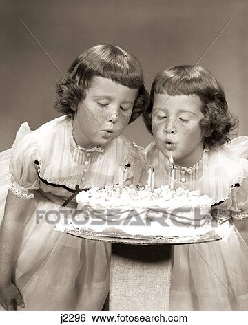 Stock Photograph - 1950s TWIN GIRLS FRECKLES BLOWING OUT CANDLES BIRTHDAY CAKE. Fotosearch