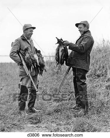 Stock Photograph - 1950s TWO MEN DUCK HUNTERS WITH SHOTGUNS ADMIRING A BRACE OF DUCKS. Fotosearch
