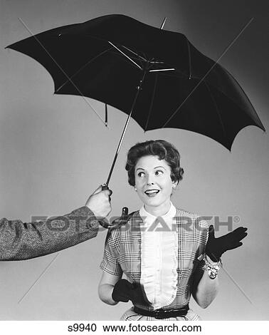 1950S Unseen Man Hold Out Umbrella To Smiling Woman In Shirtwaist Dress White Ruffled Bib Front Black Gloves And Charm Bracelet View Large Photo Image Stock Image - 1950S Unseen Man Hold Out Umbrella To Smiling Woman In Shirtwaist Dress White Ruffled Bib Front Black Gloves And Charm Bracelet. Fotosearch