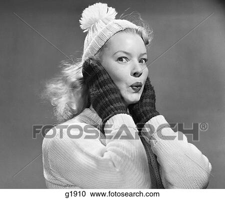Stock Image - 1950S Young Woman Pursing Lips Hands Covering Ears Looking At Camera Wearing Winter Wool Sweater Mittens Knit Cap. Fotosearch